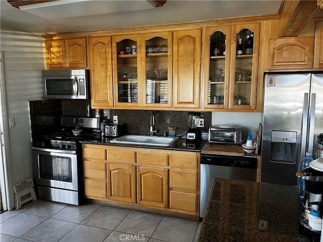 kitchen featuring a sink, stainless steel appliances, a toaster, light tile patterned floors, and glass insert cabinets