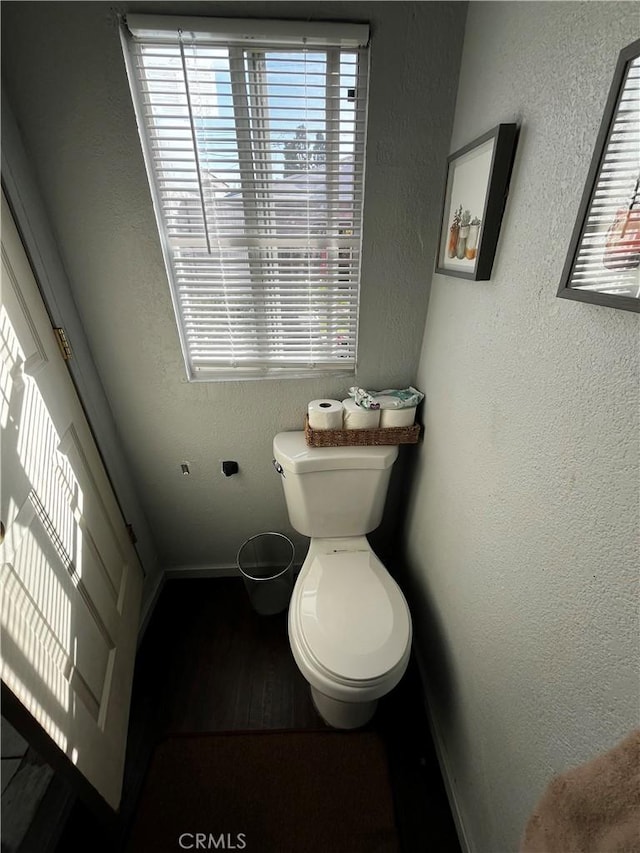 bathroom with plenty of natural light, toilet, and a textured wall