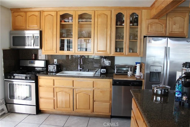 kitchen featuring a sink, dark stone counters, glass insert cabinets, and stainless steel appliances