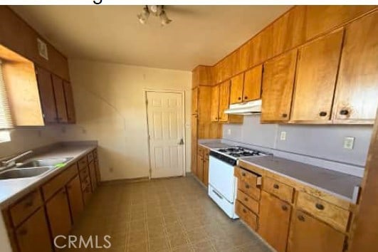 kitchen with brown cabinets, a sink, under cabinet range hood, gas range gas stove, and light countertops