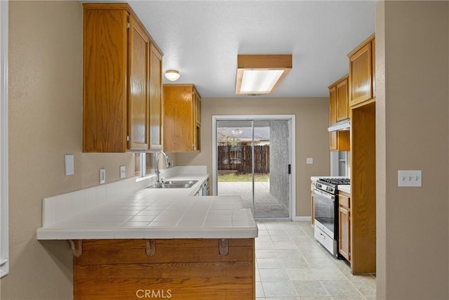 kitchen featuring under cabinet range hood, brown cabinets, stainless steel range with gas cooktop, and a sink