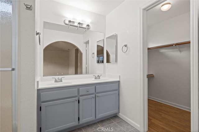 full bathroom featuring a sink, a walk in closet, baseboards, and double vanity