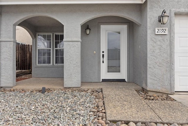 property entrance featuring stucco siding, an attached garage, and fence