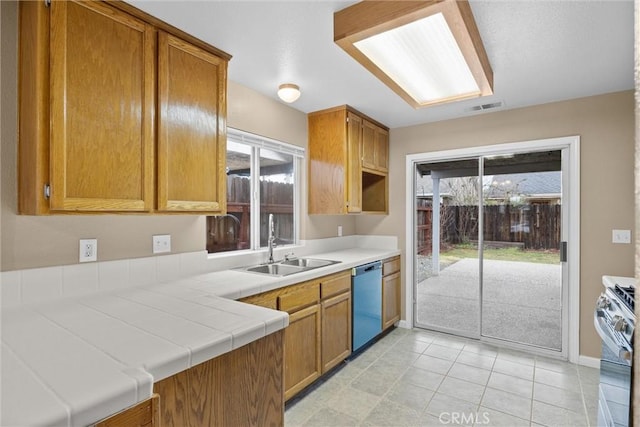 kitchen featuring visible vents, a sink, tile countertops, dishwasher, and stainless steel range with gas stovetop