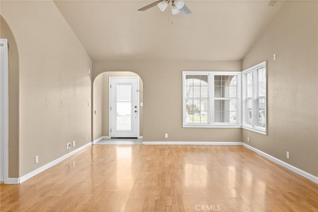 unfurnished room with baseboards, lofted ceiling, wood finished floors, arched walkways, and a ceiling fan