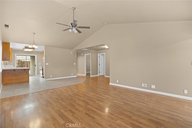 unfurnished living room with light wood finished floors, visible vents, baseboards, ceiling fan, and arched walkways