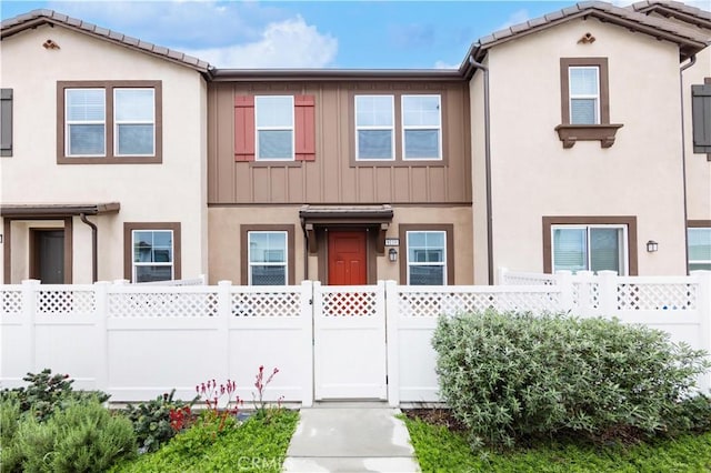 townhome / multi-family property with a tiled roof, fence, and stucco siding