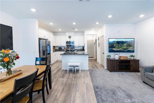 kitchen with dark countertops, open floor plan, white cabinetry, light wood-style floors, and appliances with stainless steel finishes