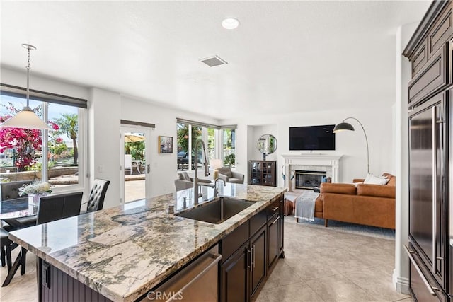 kitchen with open floor plan, an island with sink, appliances with stainless steel finishes, a fireplace, and a sink