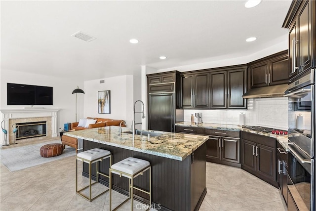 kitchen with visible vents, a breakfast bar, a sink, light stone countertops, and stainless steel gas cooktop