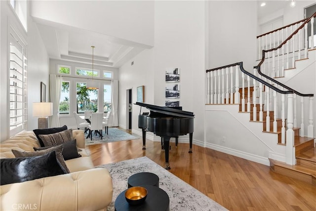 living room with stairway, wood finished floors, baseboards, a tray ceiling, and a high ceiling