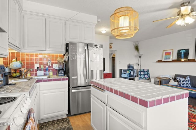 kitchen with tile countertops, light wood-style flooring, freestanding refrigerator, decorative backsplash, and white cabinetry