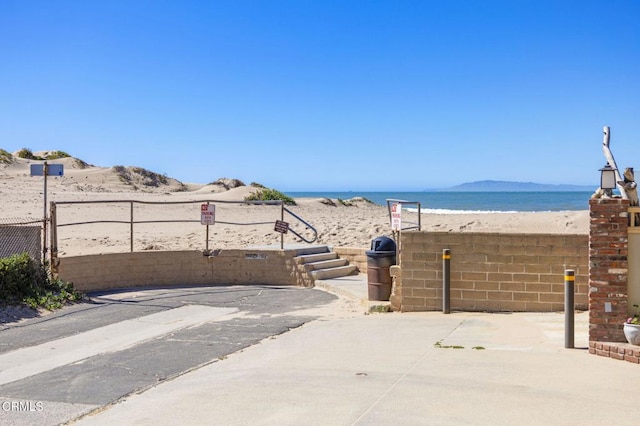 view of patio featuring fence, a beach view, and a water view