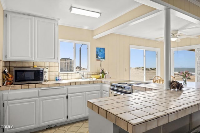 kitchen with a healthy amount of sunlight, a sink, ornamental molding, tile counters, and appliances with stainless steel finishes