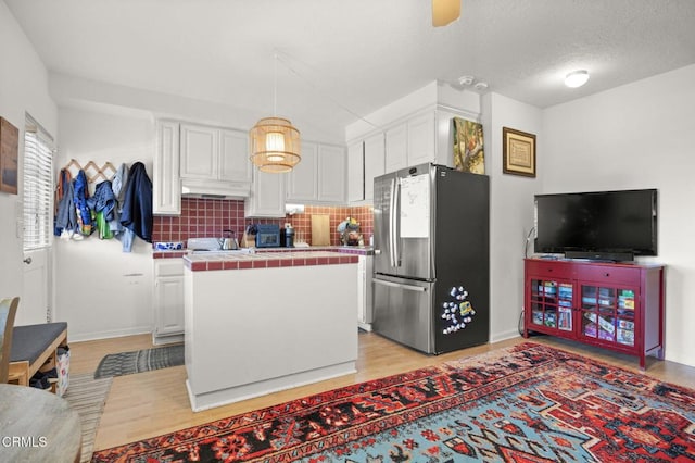 kitchen featuring a kitchen island, tile counters, under cabinet range hood, freestanding refrigerator, and white cabinets