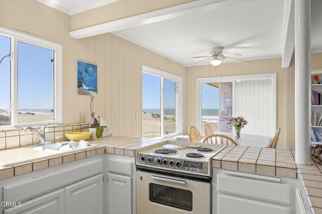 kitchen with crown molding, tile counters, white cabinets, and electric stove