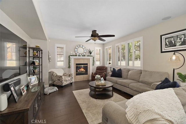 living area with a tile fireplace, ceiling fan, and dark wood-style flooring