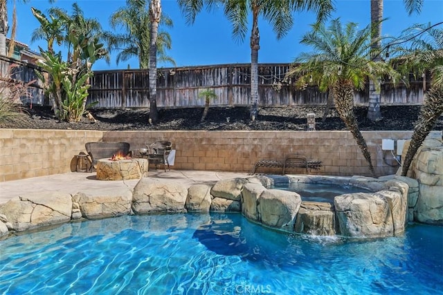 view of pool with a patio area, a fenced backyard, a pool with connected hot tub, and a fire pit