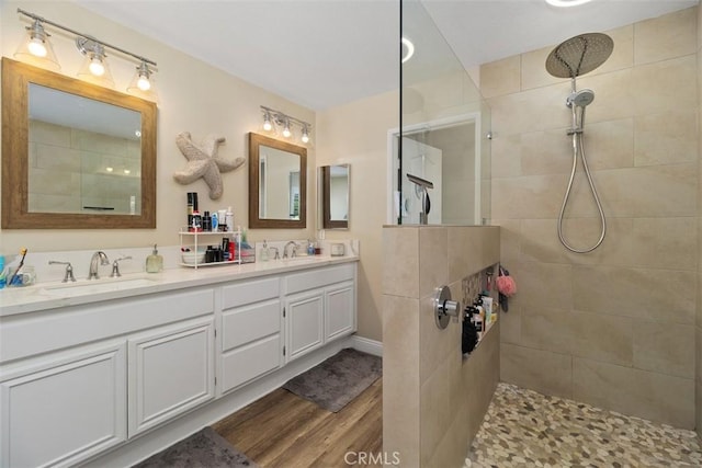 bathroom with double vanity, wood finished floors, walk in shower, and a sink