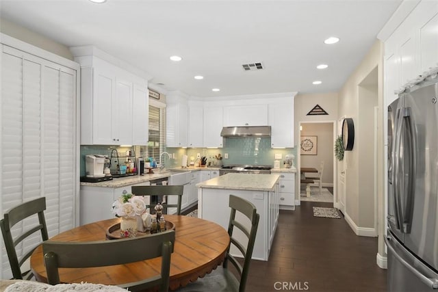 kitchen featuring visible vents, under cabinet range hood, tasteful backsplash, white cabinetry, and freestanding refrigerator