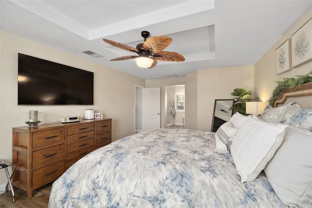 bedroom featuring visible vents, connected bathroom, a tray ceiling, wood finished floors, and a ceiling fan