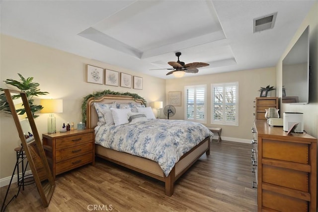 bedroom featuring visible vents, baseboards, a tray ceiling, wood finished floors, and a ceiling fan