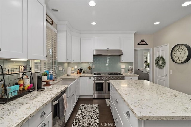 kitchen featuring under cabinet range hood, a sink, a kitchen island, range with two ovens, and light stone countertops