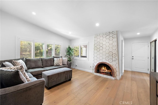 living room with light wood-type flooring, recessed lighting, baseboards, a stone fireplace, and lofted ceiling