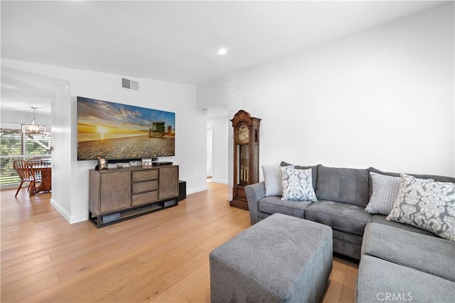 living room with light wood finished floors, visible vents, a chandelier, and baseboards