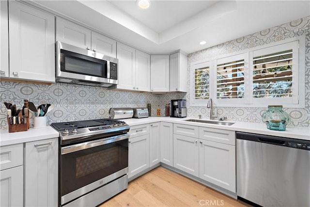 kitchen featuring a tray ceiling, a sink, stainless steel appliances, light countertops, and tasteful backsplash