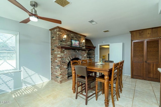 dining space featuring light tile patterned floors, visible vents, a brick fireplace, and a ceiling fan