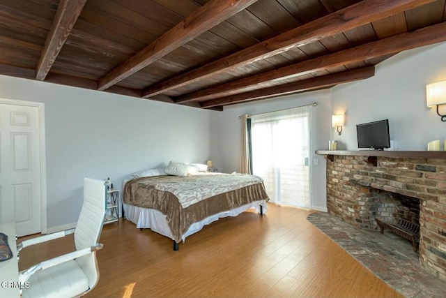 bedroom featuring beam ceiling, a brick fireplace, wooden ceiling, and wood finished floors