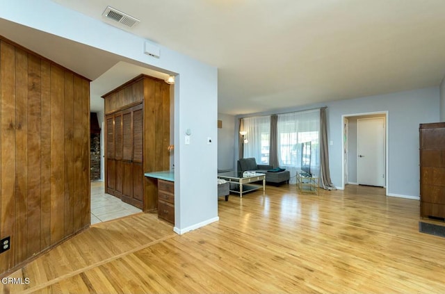 unfurnished living room with visible vents, baseboards, light wood-style floors, and wood walls