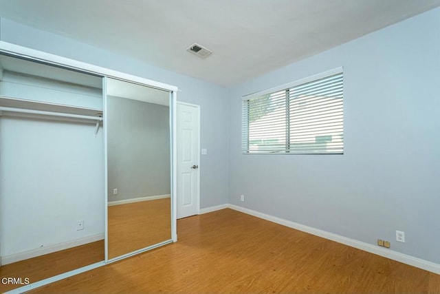 unfurnished bedroom with a closet, visible vents, baseboards, and wood finished floors