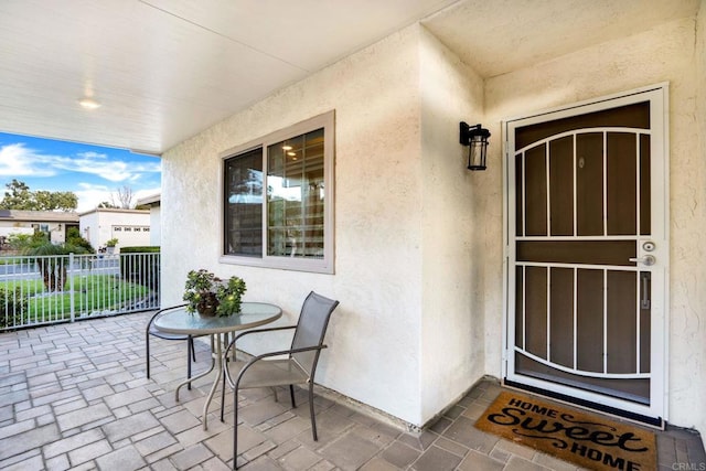 view of exterior entry featuring stucco siding, a patio area, and fence