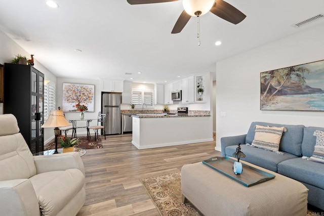 living room with light wood-type flooring, a ceiling fan, visible vents, and recessed lighting