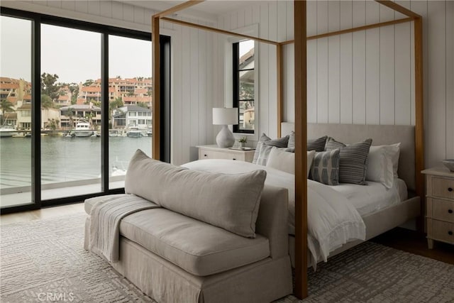 bedroom with wood finished floors, a water view, wooden walls, and access to exterior