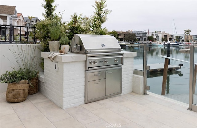 view of patio featuring a water view, a grill, exterior kitchen, and a dock