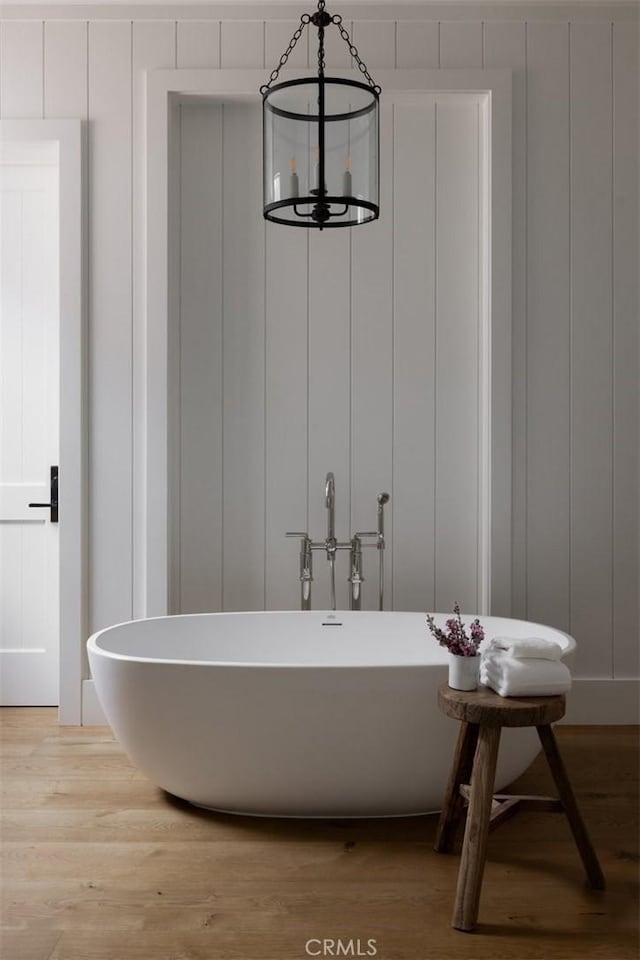 bathroom with a freestanding tub, wood finished floors, and a decorative wall