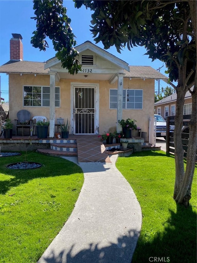 bungalow-style home with covered porch, stucco siding, a chimney, and a front lawn