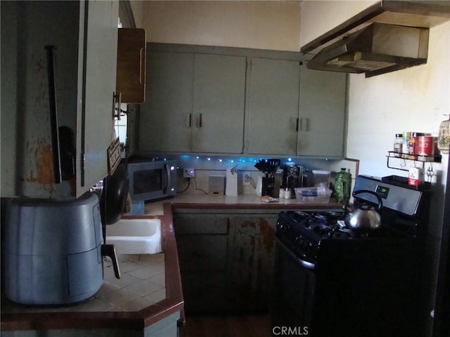 kitchen with black gas range, stainless steel microwave, freestanding refrigerator, and tile patterned flooring