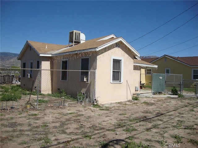 back of property with a gate, stucco siding, central AC, and fence