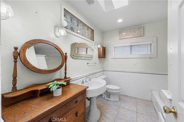 bathroom with tile patterned flooring, visible vents, wainscoting, a skylight, and a sink