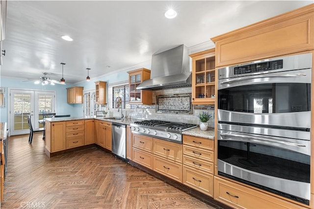 kitchen with glass insert cabinets, decorative backsplash, appliances with stainless steel finishes, a peninsula, and wall chimney exhaust hood