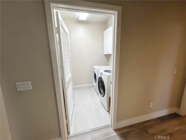 clothes washing area with light wood finished floors, baseboards, cabinet space, and washing machine and clothes dryer