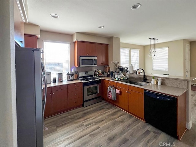 kitchen featuring light wood finished floors, brown cabinets, appliances with stainless steel finishes, a peninsula, and a sink