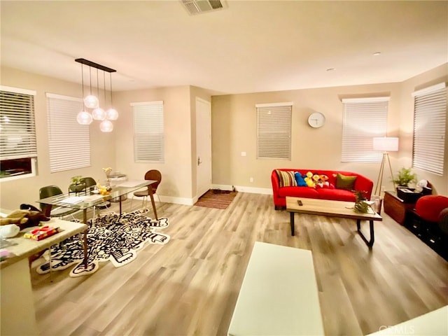 living room with light wood-type flooring, visible vents, baseboards, and a chandelier