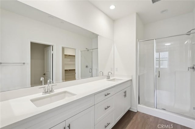 full bathroom with a sink, double vanity, wood finished floors, and a shower stall