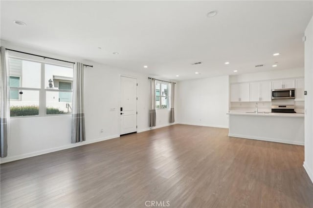 unfurnished living room featuring recessed lighting, wood finished floors, baseboards, and a sink