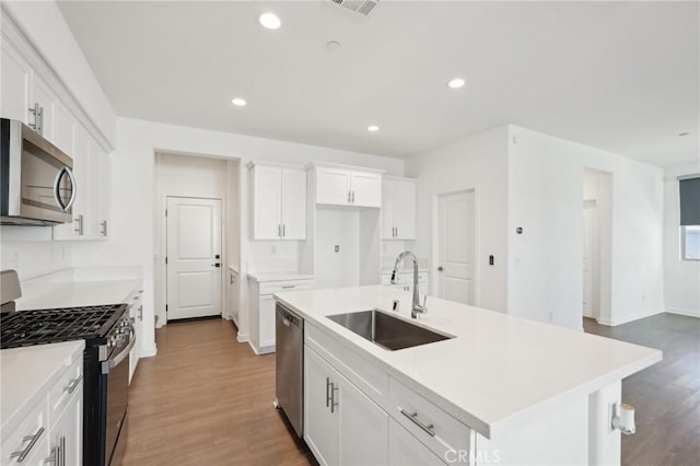 kitchen featuring recessed lighting, appliances with stainless steel finishes, wood finished floors, white cabinets, and a sink